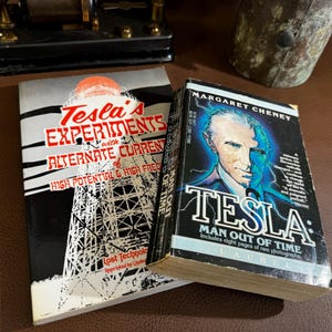 May include: Two books about Nikola Tesla. The book on the left is titled "Tesla's Experiments with Alternate Current of High Potential & High Frequency". The book on the right is titled "Tesla: Man Out of Time" by Margaret Cheney.