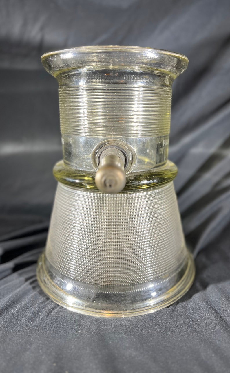 May include: A clear glass bottle with a textured surface and a metal spout. The bottle has a wide base and a narrow neck. The bottle is designed for dispensing liquids.