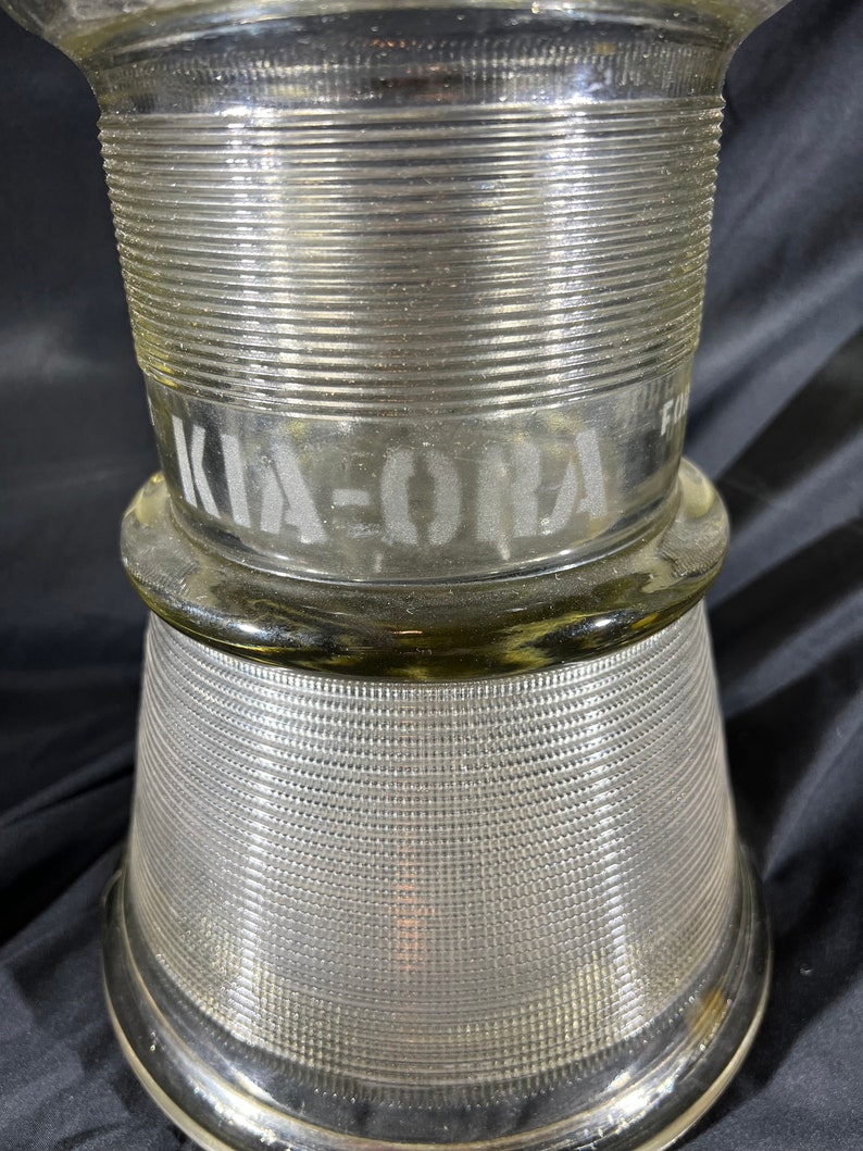 May include: A clear glass jar with a textured surface and the word "KIA-ORA" etched on the side.
