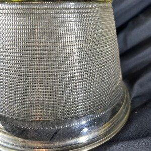 May include: A clear glass lampshade with a textured, grid-like pattern. The shade has a wide, flared base and a narrow top.