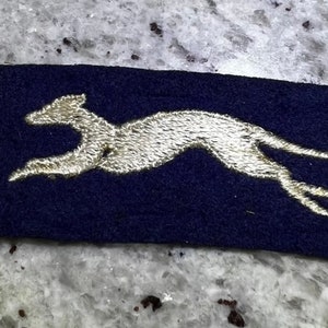May include: A blue fabric patch with a white embroidered image of a running greyhound.