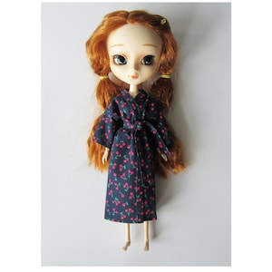 May include: A red-haired doll wearing a blue and red cherry print robe. The doll has blue eyes and a light complexion.