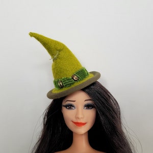 May include: A green felt witch hat with a brown brim and green velvet trim. The hat has a pointed crown and is decorated with small gold buttons.