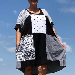 May include: A patchwork dress with a black, white, and gray color scheme. The dress features various patterns, including hearts, text, and gingham. It has short sleeves and pockets. The dress is knee-length and appears to be made of a soft fabric.