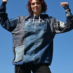 May include: A long-sleeve hooded sweatshirt featuring a patchwork design of blue denim and dark blue knit fabric. The front includes a denim pocket and a hood with white drawstrings. The sleeve displays the text USSELL and 190 in white lettering.