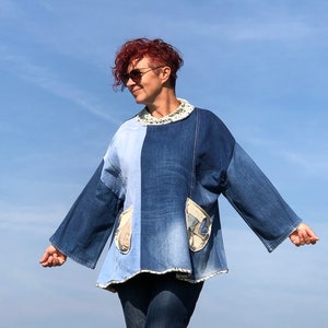 May include: A woman wearing a blue denim jacket with patchwork details and a white collar. The jacket has large pockets on the front and long sleeves. The woman is standing in front of a blue sky.