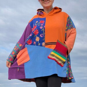 May include: A colorful patchwork hoodie with a floral embroidered design. The hoodie is made of a soft, comfortable fabric and has a relaxed fit. The hoodie is orange, blue, purple, and green.