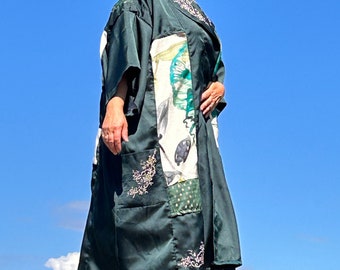 May include: A green, long-sleeved,  patchwork kimono with floral embroidery. The kimono has a white and green floral pattern on the front and a green and white polka dot pattern on the back. The kimono is worn by a person with red hair and sunglasses.