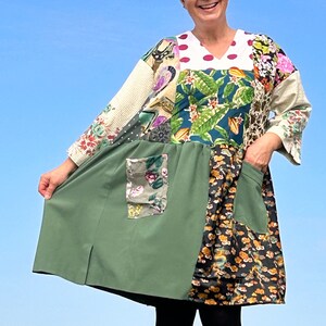 Op de afbeelding: Een patchworkjurk met een groene, bloemige en witte print. De jurk heeft een witte kraag en een V-hals. De jurk heeft twee zakken aan de voorkant.
