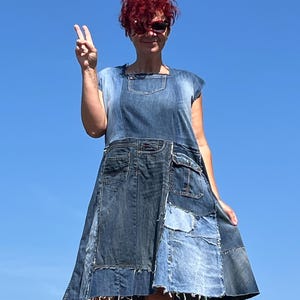 May include: A patchwork denim dress with a square neckline and cap sleeves. The dress is made from various shades of blue denim, with pockets and a flared skirt. The background is a clear blue sky.