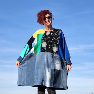 Könnte beinhalten: Eine blaue, grüne, gelbe und schwarze Patchwork-Tunika mit einem Jeansrock. Die Tunika hat einen Weltraum-Print mit Planeten und Sternen.