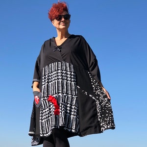 May include: A black and white patterned tunic dress with a V-neck and short sleeves. The dress features a mix of patterns, including a black and white geometric print, polka dots, and a red accent. The model is wearing sunglasses.