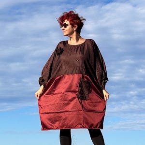 Peut inclure: Une robe surdimensionnée avec un design color-block distinctif. La partie supérieure présente un motif à carreaux marron, tandis que la section inférieure est de couleur bordeaux unie. La robe a des manches longues et une coupe décontractée.