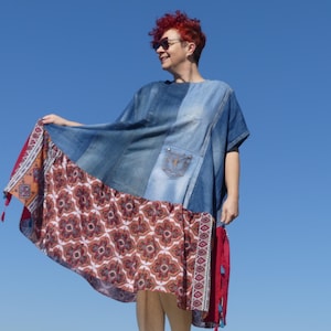Op de afbeelding: Een blauwe denim jurk met een rode en witte geruite rok. De jurk heeft een losse pasvorm en een ronde hals. Het model draagt een zonnebril en heeft rood haar.