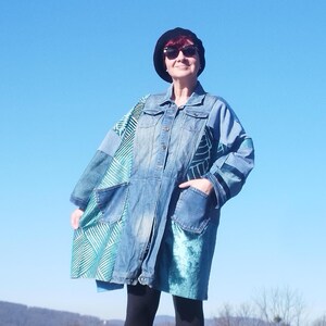 May include: A blue denim jacket with a green and blue patterned lining. The jacket has a button closure and two pockets. The person wearing the jacket is wearing a black beret and sunglasses.