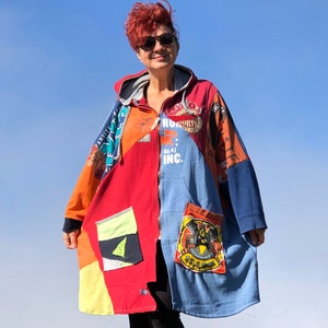 Puede incluir: Una sudadera con capucha de patchwork colorida con cierre de cremallera y capucha. La sudadera está hecha de diferentes telas y tiene varios parches y logotipos, incluyendo "Arctic" y "Truckin' Inc."