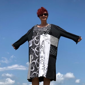 May include: A patchwork dress with a black top and long sleeves. The dress features a variety of black and white patterns, including polka dots, geometric shapes, and abstract designs. The sleeves have a ruffled edge. The background is a clear blue sky.
