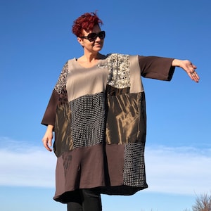 Peut inclure: Une robe en patchwork marron, beige et noir à manches longues et à la coupe ample. La robe est faite de différents tissus, dont un coton marron, une soie beige et un velours noir. La robe est portée par une personne aux cheveux roux et aux lunettes de soleil.