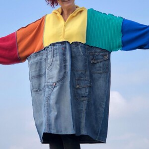 Peut inclure: Une veste en patchwork colorée faite de denim, de polaire et de tissu rayé. La veste a un motif arc-en-ciel et une fermeture éclair.
