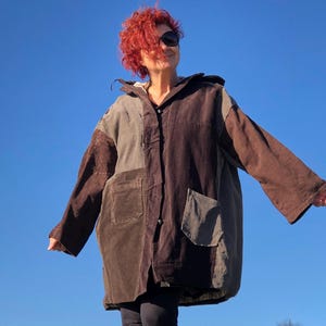 May include: A brown, gray, and beige patchwork jacket with a hood. The jacket has large pockets and a button closure.