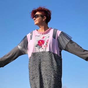 Può includere: Una donna indossa un vestito a strati rosa e grigio con una stampa floreale. Il vestito ha una vestibilità ampia e una gonna lunga e fluida. La donna indossa occhiali da sole e ha i capelli corti e rossi.