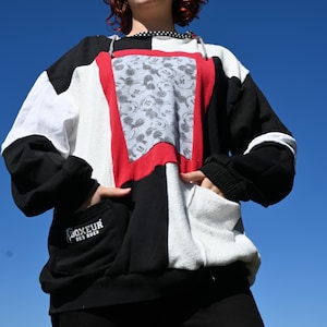 May include: A colour-blocked hooded sweatshirt featuring black, white, and red panels. The centre panel displays a grey Mickey Mouse pattern. A black pocket on the lower left features the white text BOXEUR DES RUES. It has a black and white polka dot hood lining.