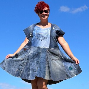 Op de afbeelding: Een vrouw draagt een spijkerrok gemaakt van hergebruikte spijkerbroeken. De rok heeft meerdere zakken en een patchwork-design. Ze staat voor een blauwe lucht.