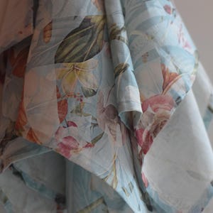 May include: A blue and white floral fabric with a delicate pattern of flowers and leaves. The fabric is folded and draped, showcasing the intricate design.