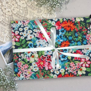 Könnte beinhalten: Eine Geschenkbox mit Blumenmuster und einem weißen Satinband, das zu einer Schleife gebunden ist. Die Box ist in ein dunkelblaues Stoff mit einer Vielzahl von bunten Blumen eingewickelt.