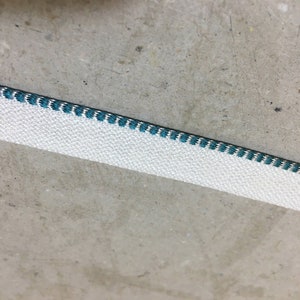 May include: White fabric trim with a teal blue stitched edge.