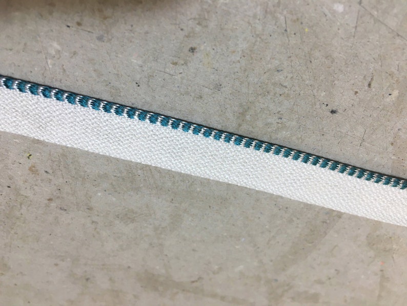 May include: White fabric trim with a teal blue stitched edge.