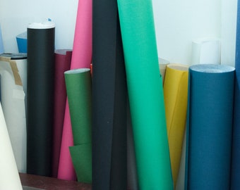 May include: A collection of colorful fabric rolls in various shades, including black, pink, green, and blue. The rolls are tightly wound and stand upright, creating a visually appealing display of textiles.