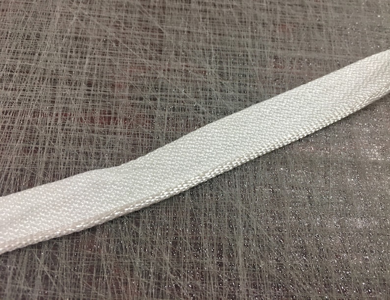 May include: A white, woven fabric ribbon with a slightly textured surface.