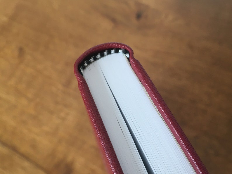 May include: Close-up of the spine of a burgundy hardcover book with a black and white patterned edge.