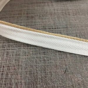 May include: White cotton ribbon with a gold trim. The ribbon is flat and has a woven texture.
