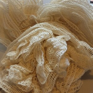 May include: A close-up of a white crocheted mesh bag, with a ruffled texture. The bag is made of a delicate, open-weave material.