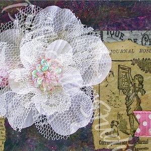 Puede incluir: Una flor de encaje blanco con un centro de lentejuelas rosa e iridiscente. La flor está sobre un fondo de papel estampado marrón, morado y blanco con el texto "JOURNAL ROSE" visible.