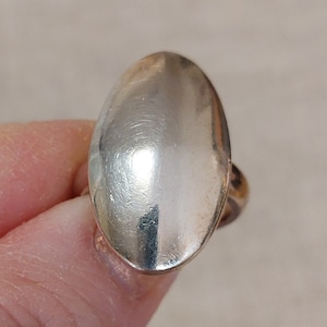 Puede incluir: Un anillo de plata de forma ovalada con una superficie lisa y pulida.