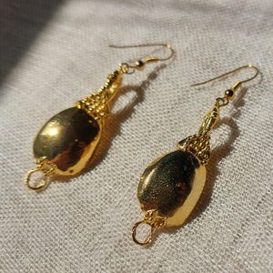 Puede incluir: Un par de pendientes dorados. Cada pendiente presenta un colgante dorado pulido en forma de l&aacute;grima, suspendido de una parte superior dorada texturizada y decorativa. Los pendientes tienen un cierre de gancho simple.