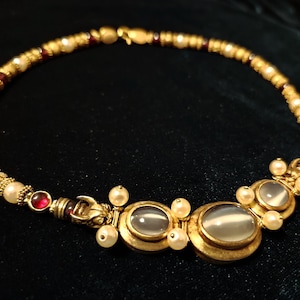 Puede incluir: Un collar de oro con una cadena de cuentas y un colgante con tres piedras ovaladas de color blanco lechoso.