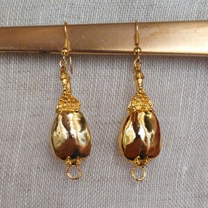 Puede incluir: Un par de pendientes dorados con forma de l&aacute;grima. Los pendientes tienen una parte superior texturizada y un cuerpo liso y brillante. Cuelgan de un gancho dorado y tienen un peque&ntilde;o anillo en la parte inferior.