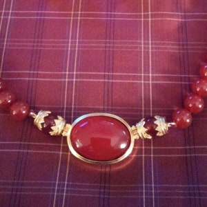 May include: A red gemstone necklace with a large oval-shaped red gemstone pendant set in gold.