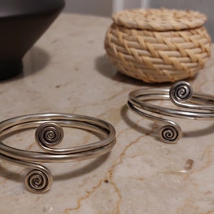 May include: Two silver bracelets with a spiral design. The bracelets are made of thin metal and have a simple, elegant look.