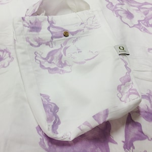 May include: A white tote bag with a purple floral print. The bag has a wooden button closure and a small green label with the text "Q Fitting".