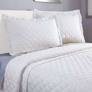 May include: White quilted bedspread with two white quilted pillowcases. The bedspread and pillowcases have a diamond pattern.