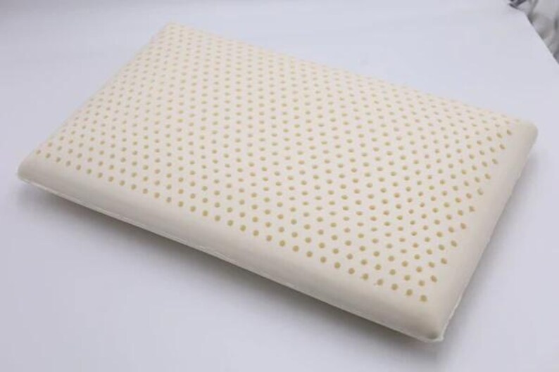 May include: A white latex pillow with a pattern of small holes. The pillow is designed for sleeping and is made of a breathable material.