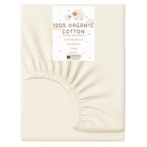 May include: Cream-colored crib mattress protector made of 100% organic cotton. The product features a water-resistant design and includes a label with text and a sheep illustration. The fitted sheet is folded.
