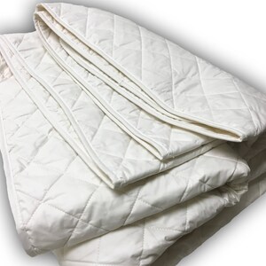 May include: A white quilted mattress pad folded in thirds. The pad has a diamond pattern and is made of a soft, breathable fabric.