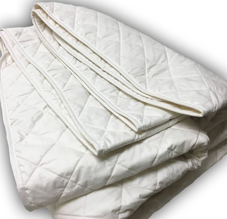 May include: A white quilted mattress pad folded in thirds. The pad has a diamond pattern and is made of a soft, breathable fabric.