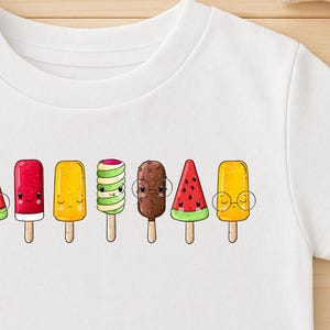 Könnte beinhalten: Weißes T-Shirt mit einer Reihe bunter Cartoon-Eis am Stiel. Die Eis am Stiel umfassen Schokoladen-, Wassermelonen-, Kirsch-, Zitronen- und Kiwiaromen. Das Shirt wird mit Jeansshorts und Leinenschuhen auf einer Holzoberfläche gezeigt.
